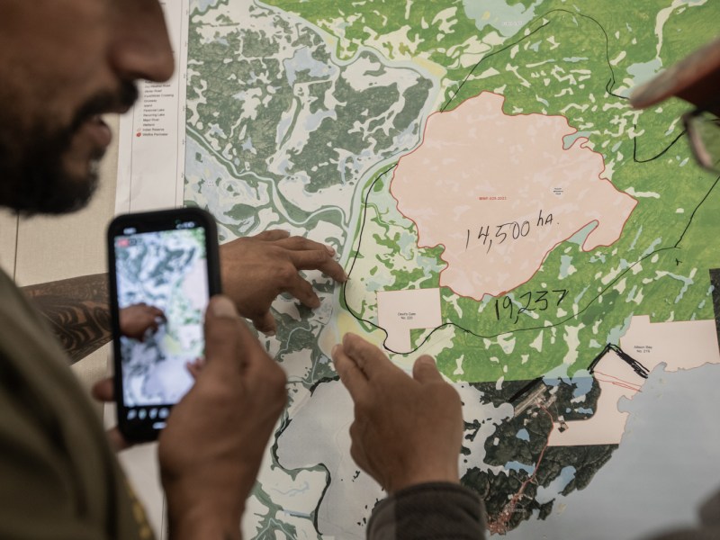 Two men stand in front of a map of the Lake Athabasca area, where the wildfires are burning. Only their hands and parts of their faces are visible