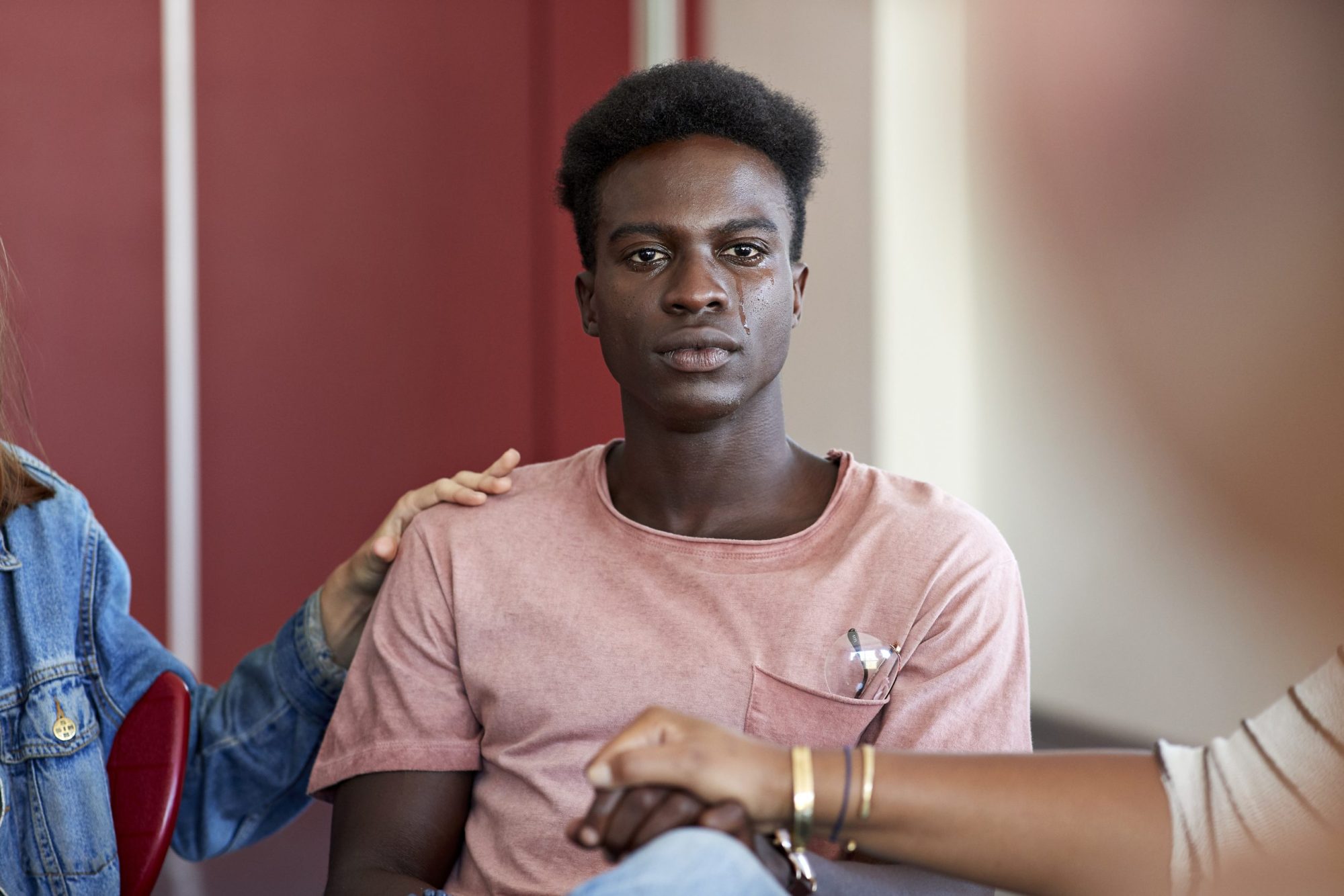 Sad young man crying while being consoled by female friends sitting in classroom during group therapy meeting at university