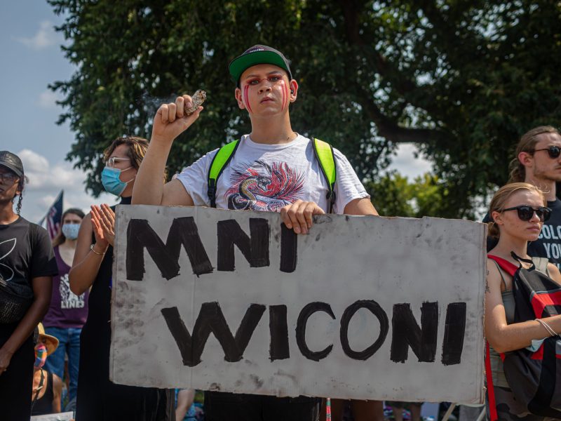 A young person holds a sign that reads "Mni Wiconi."