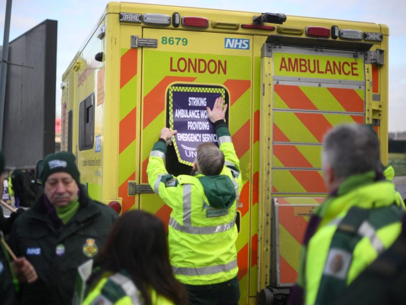 An ambulance worker sticks a cardboard sign on an ambulance as he takes part in a rally at a picket line outside the Docklands Emergency Operating Centre.