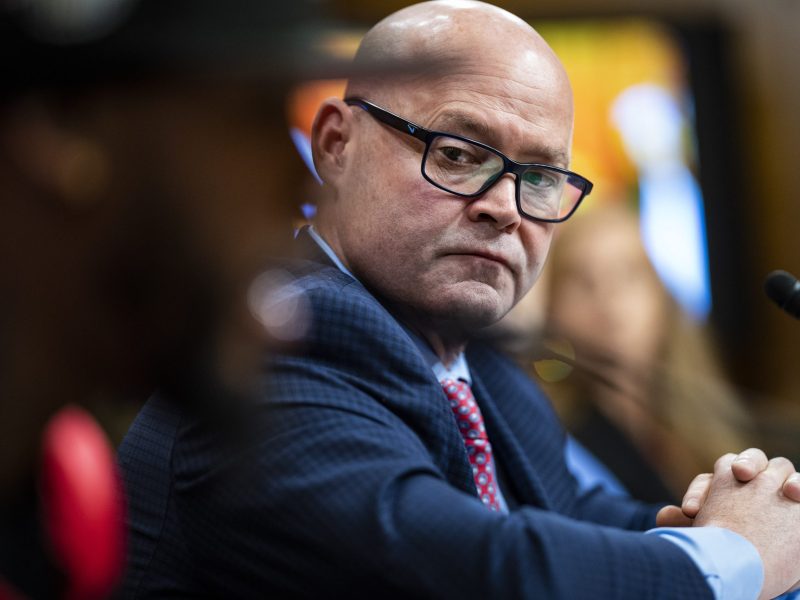 In the foreground, Amazon Labor Union president Christian Smalls can be seen out of the camera's focus. Behind him, in focus, is Sean O'Brien. Sean is middle-aged, bald, bespectacled, and white. He has a blue suit on a maroon tie.