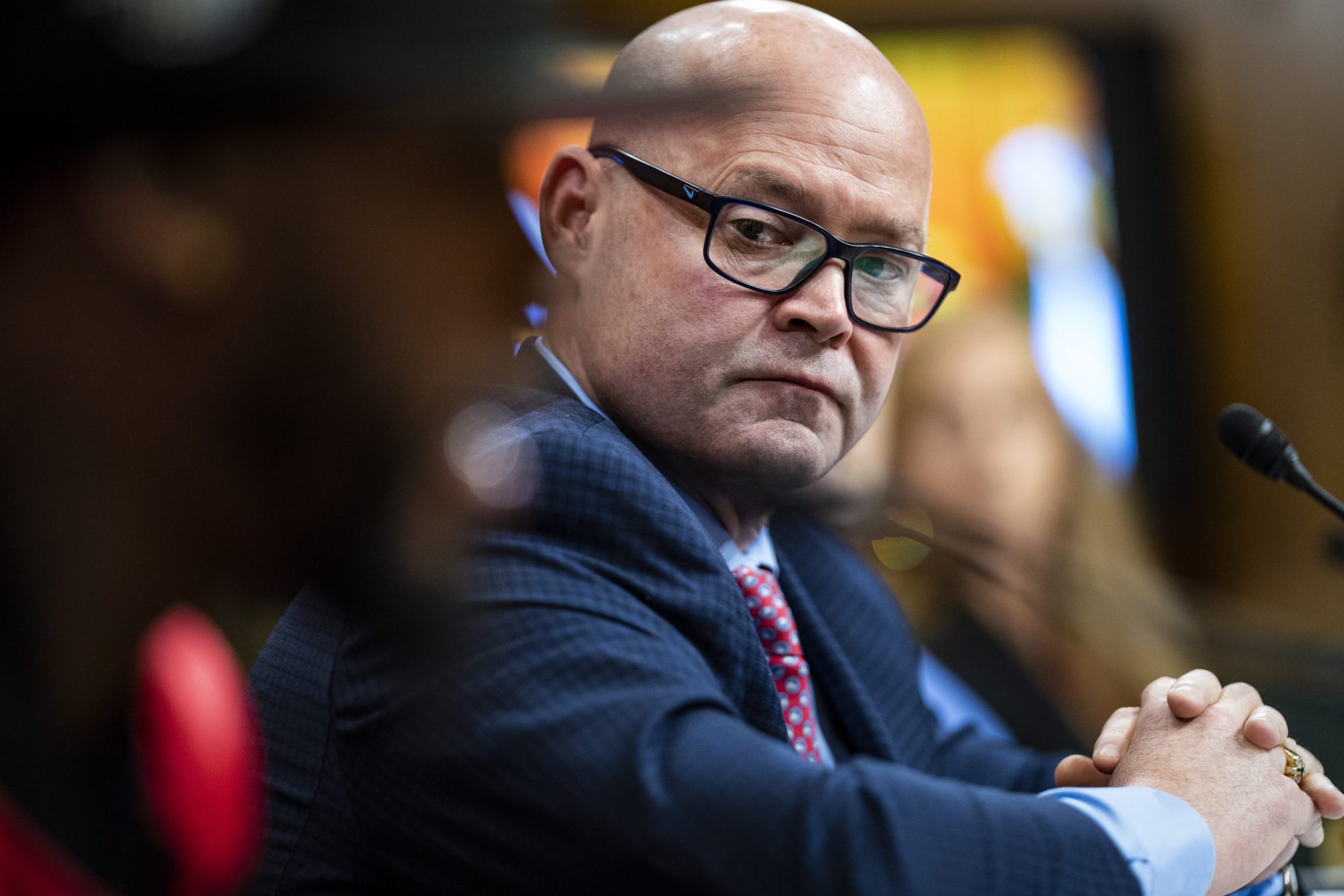 In the foreground, Amazon Labor Union president Christian Smalls can be seen out of the camera's focus. Behind him, in focus, is Sean O'Brien. Sean is middle-aged, bald, bespectacled, and white. He has a blue suit on a maroon tie.