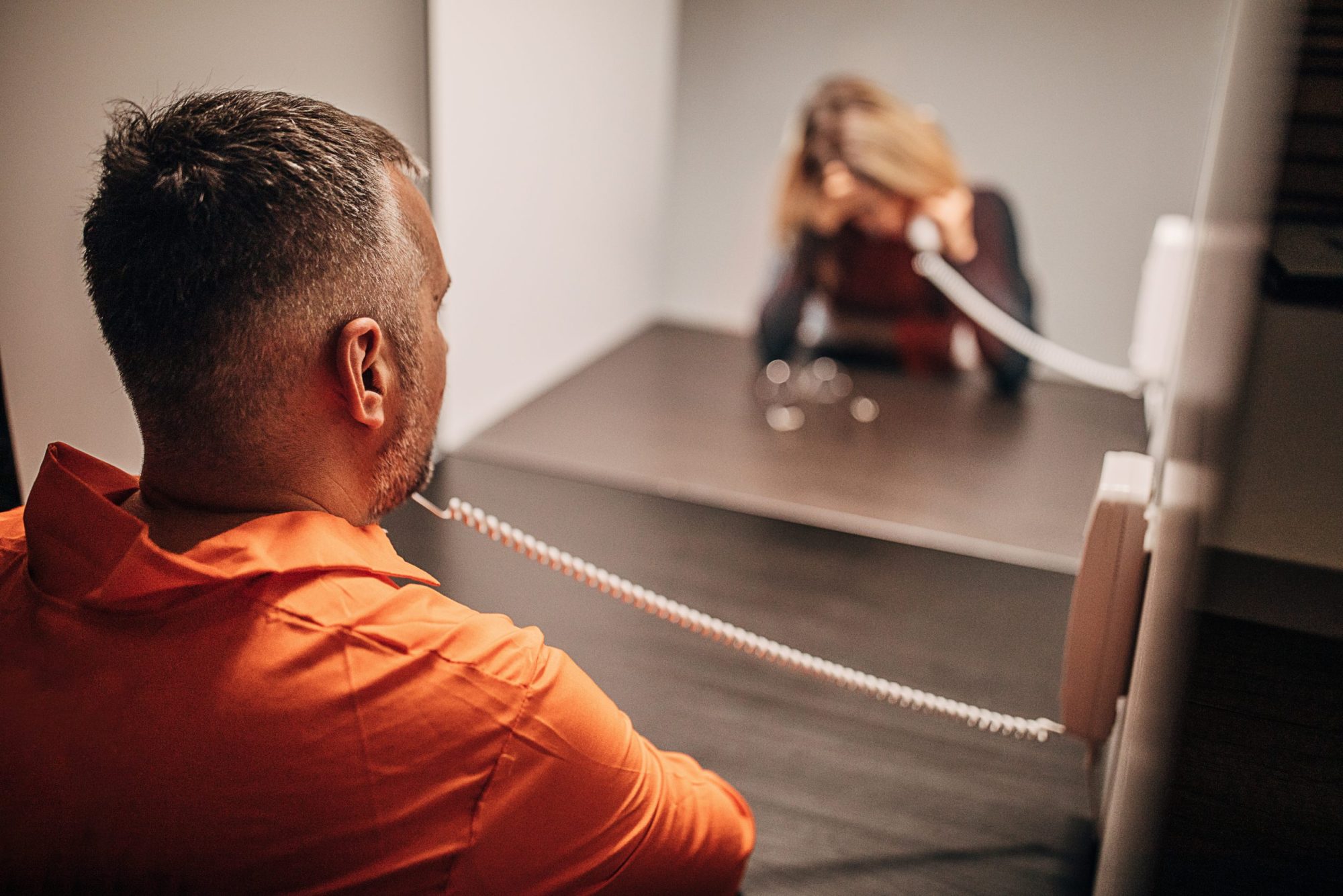 Male prisoner talking over the phone with his wife in prison visit room.
