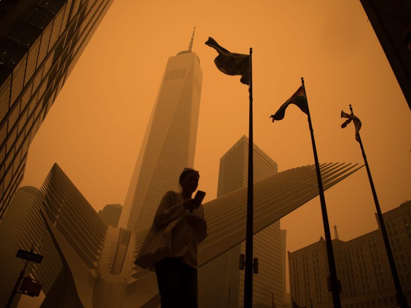 Low angle shot of a pedestrian walking in front of a skyscraper, the entire scene is shrouded in an eerie orange smog.