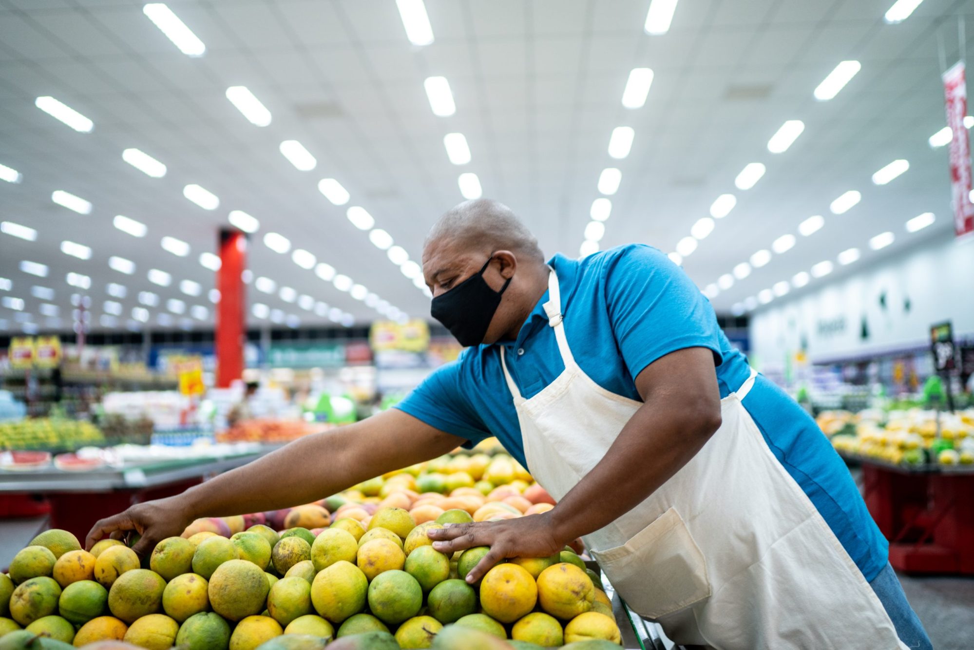 Man wearing face mask working arranging fruits in a supermarket