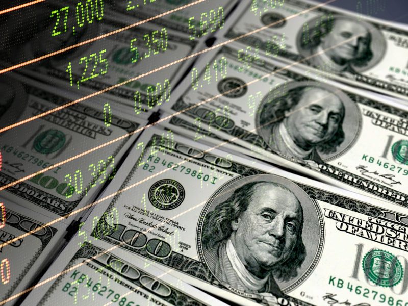 100 dollar bills and stock market data dashboard via Getty Images