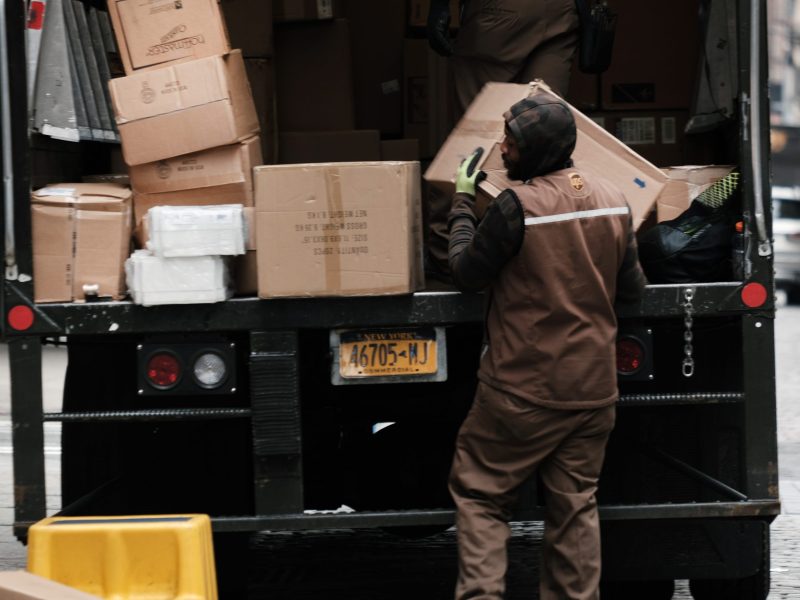 A UPS delivery driver unloads packages out of the back of a delivery truck.