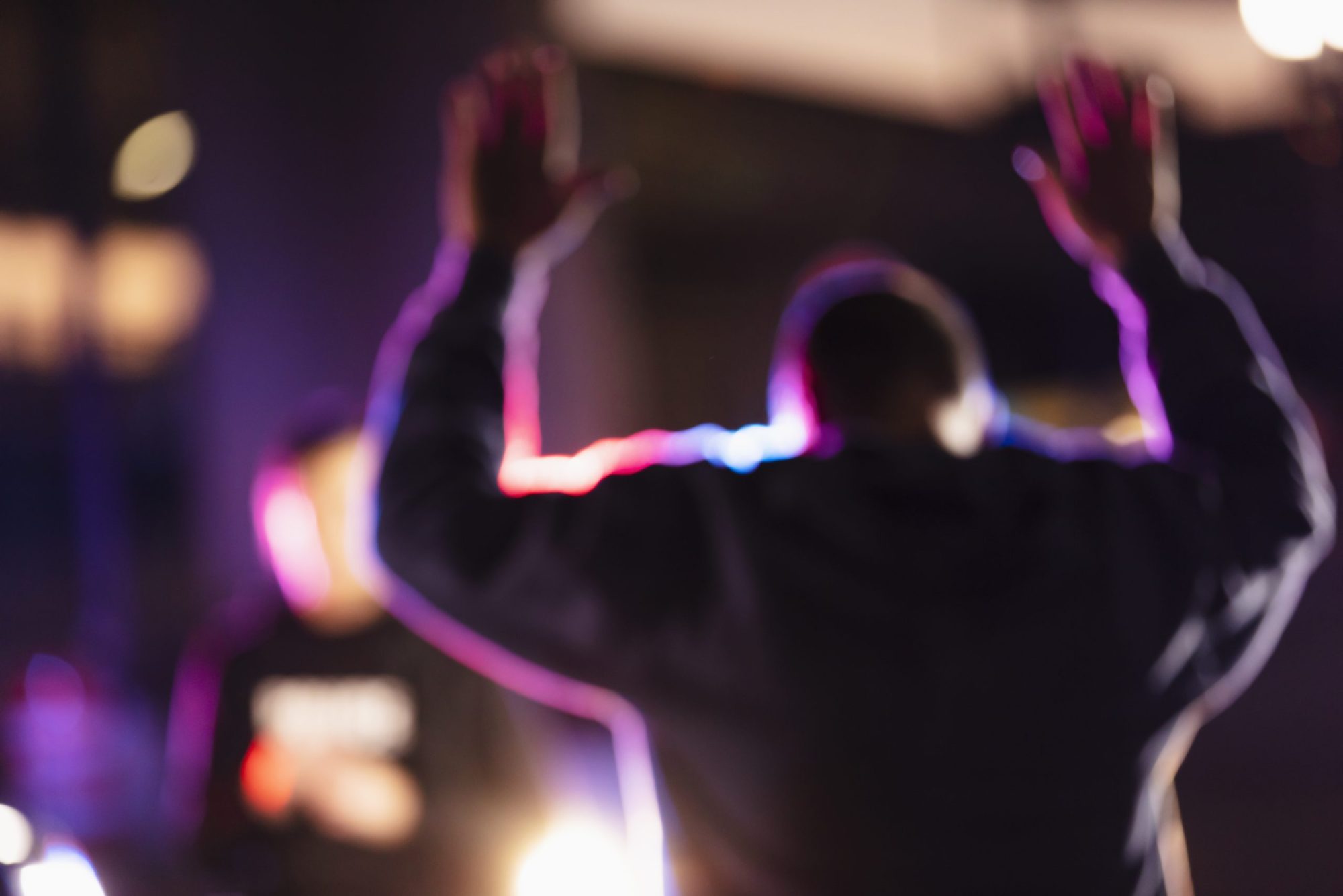 A man with his hands raised, surrendering to police at night. His back is to the camera. A policewoman is standing in the background facing the suspect.