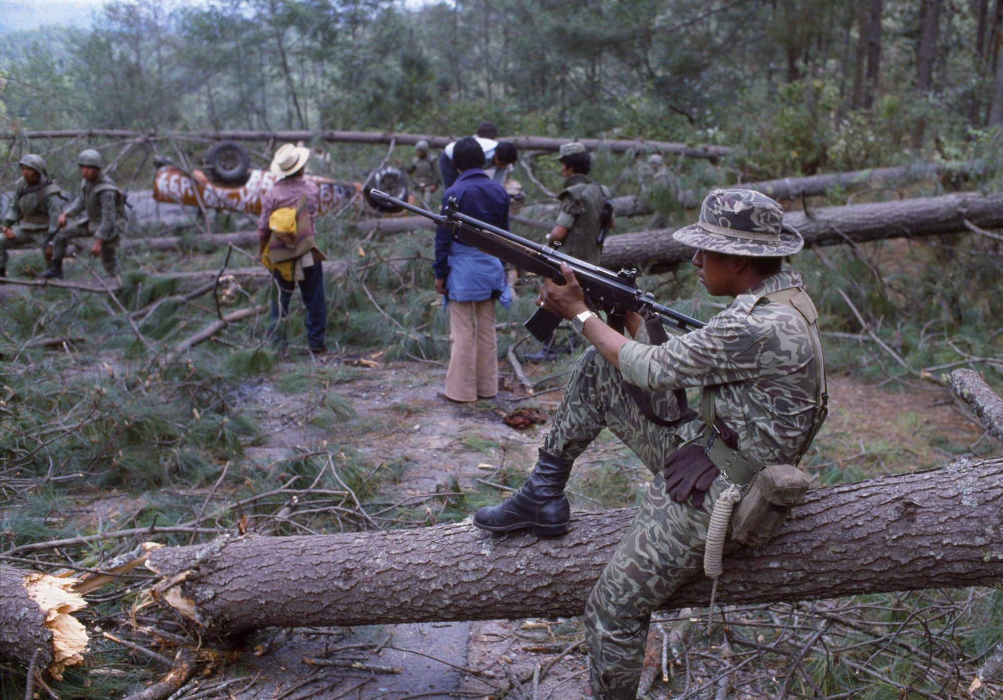 View of a Guatemalan Army soldier as he sits on a felled tree on a section of the Pan American Highway, Los Encuentros, Guatemala, March 7, 1982. Photo by Robert Nickelsberg/Getty Images