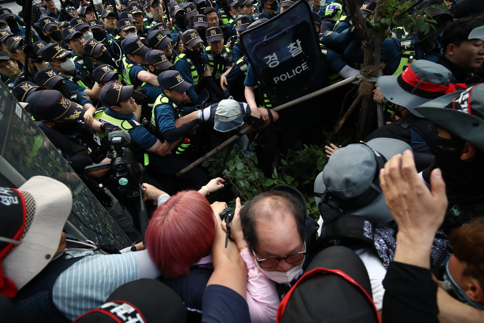 A wave of riot-shield wielding police officers descends upon a group of trade unionists, who have their arms raised in self defense.