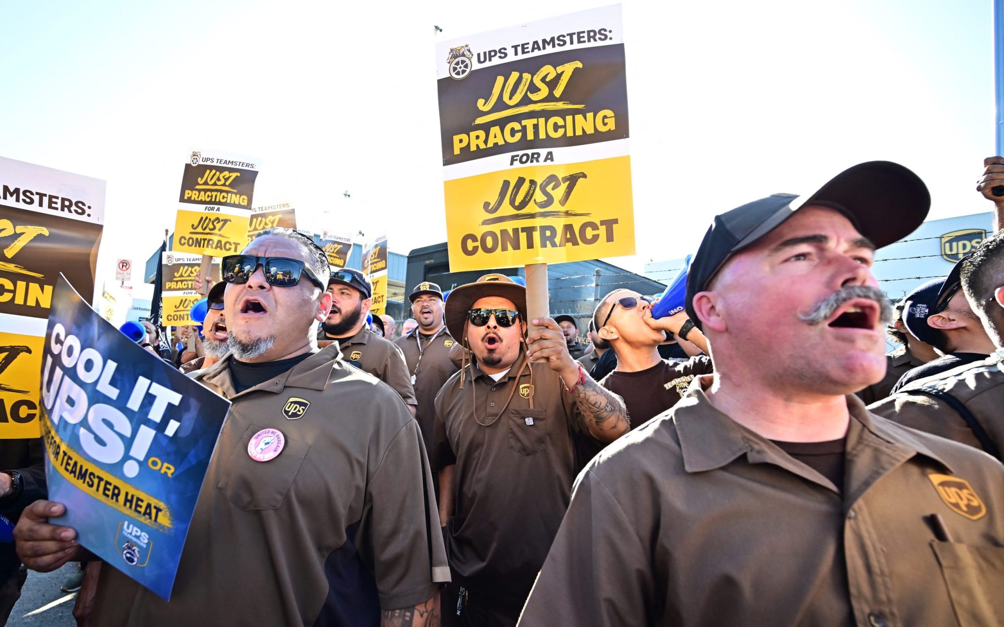 UPS workers in their uniforms carrying practice picket signs on a sunny day