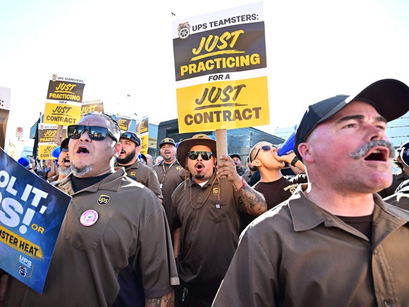 UPS workers in their uniforms carrying practice picket signs on a sunny day