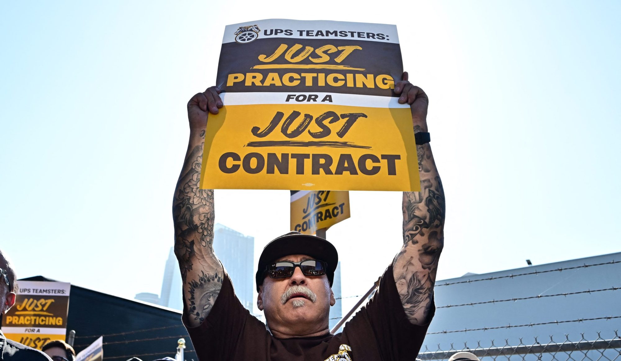 UPS workers hold placards reading "Just Practicing for a Just Contract" at a practice picket held by the Teamsters Union on July 19, 2023, in Los Angeles, California, ahead of the August 1st deadline for the Teamsters and UPS to reach an agreement on a new contract.