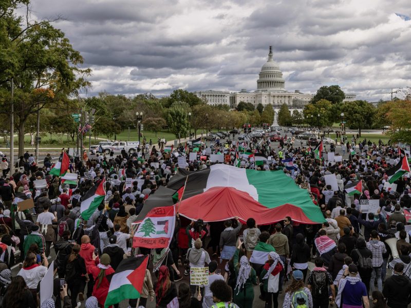 A large crowd marching towards Capitol Hill carries a massive Palestinian flag