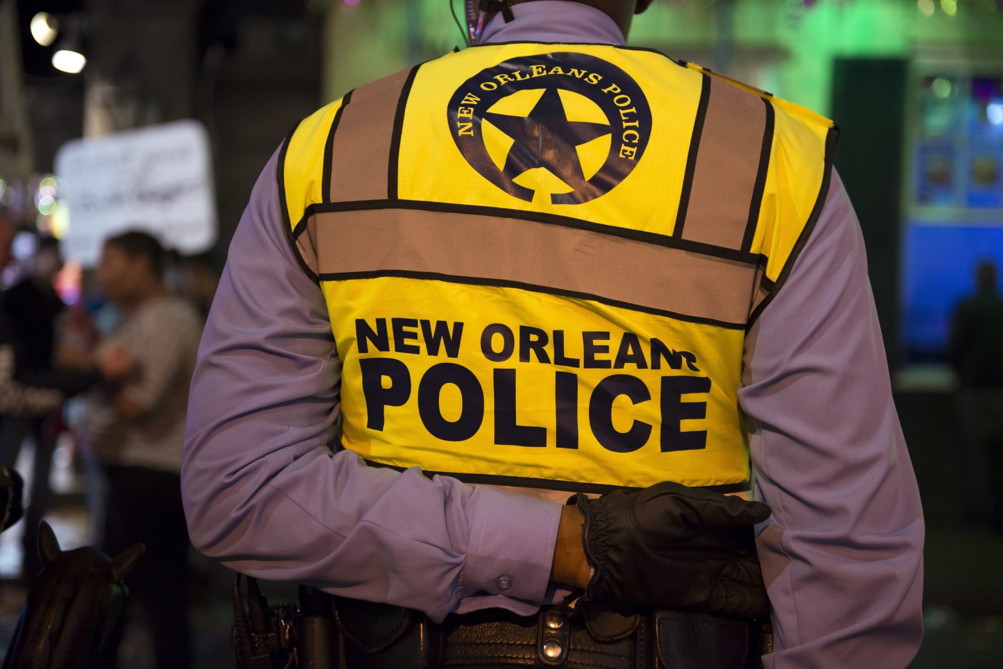The back of a uniformed police officer wearing a vest that reads "New Orleans Police"