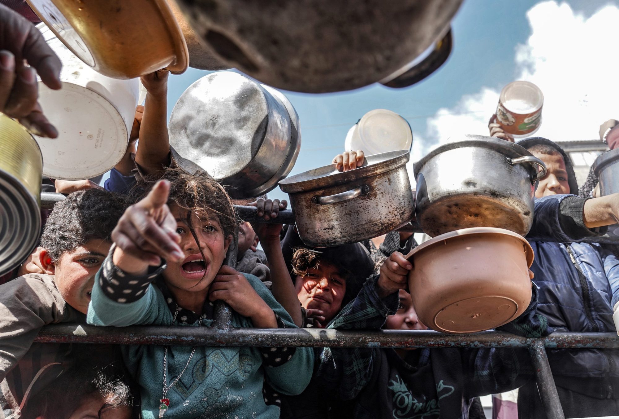 Palestinian children, holding empty pots, wait in line to receive food prepared by volunteers for Palestinian families, displaced to Southern Gaza due to Israeli attacks, between rubble of destroyed buildings in Rafah, Gaza, on Feb. 10, 2024.