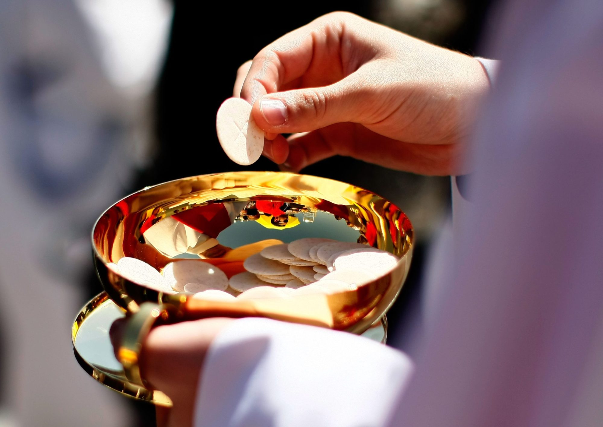 A hand holding a wafer over a gold bowl.