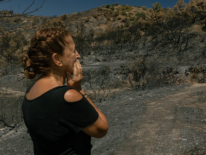 Eleni Diacogiannis Pelekanos stands in disbelief, with her hand covering her mouth, as she surveys the charred hills and trees surrounding her former home in the village of Asklipio, Greece. Photo taken by Vasily Krestyaninov on Aug. 8, 2023.