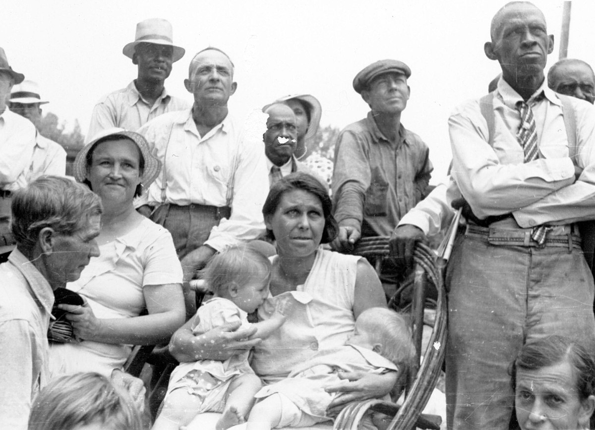 Men, women, and children, black and white, listen to a speaker at an outdoor Southern Tenant Farmers Union meeting, 1937. Wikimedia Commons